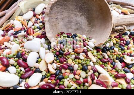A wooden scoop rests above a colorful mixture of dried beans, chickpeas, lentils and peas in a lined wicker basket. Stock Photo