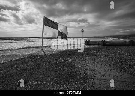 A 'safe to swim' flag flying in the onshore breeze at Borth, Ceredigion, Wales. A black and white/monochrome image. Stock Photo