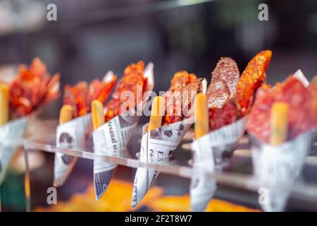 Traditional Spanish tapas at the grocery market. Envelopes with slices of different types Spanish salami . Selective focus, bokeh. Stock Photo