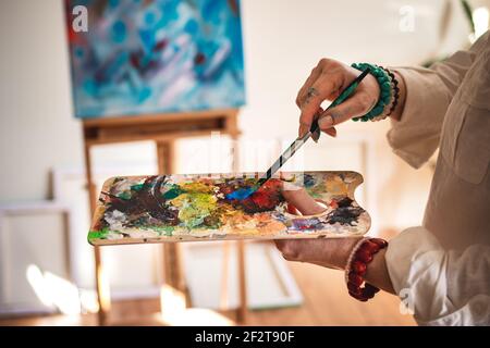 Artist mixing acrylic colors at palette and working on abstract paintings. Woman working in her art studio. Learning creative skill and technique Stock Photo