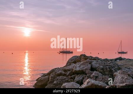 Beautiful sunset view on Lake Garda with sailing boats and textured stones in the foreground. Lake garda, Italy Stock Photo