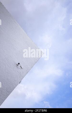 Minimalistic photo, Wall of a house with a security camera against the cloudy sky. Stock Photo