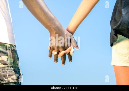 Multiracial couple walking hand in hand against a blue sky - Concept of multi ethnic love over social barriers Stock Photo