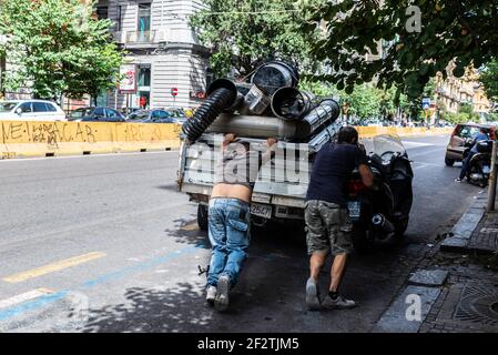 Naples, Italy - September 9, 2019: Two men pushing a damaged van full of junk while one talks on the mobile phone on a street in the old town of Naple Stock Photo