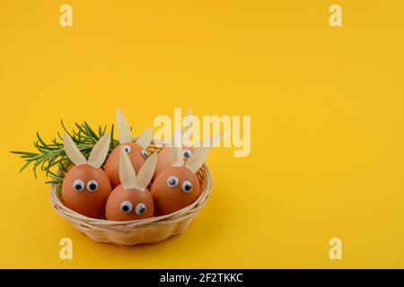 Easter eggs with eyes and rabbit ears in an wicker basket. Copy space. Happy Easter concept. Stock Photo