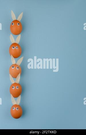 Easter Eggs with eyes and Rabbit ears in a Row on blue background. Vertical, copy space. Happy Easter concept. Stock Photo