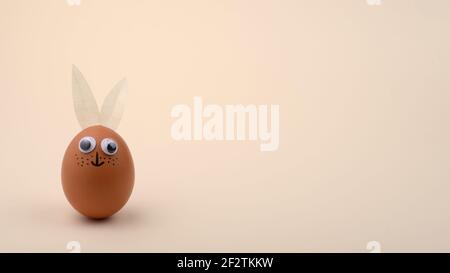 One Easter egg with eyes and rabbit ears on beige horizontal background. Copy space. Happy Easter concept. Stock Photo