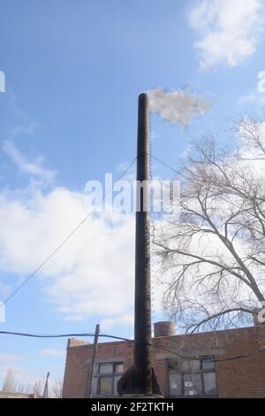 Old building is boiler room. Black large chimney with dark smoke against blue sky. Environmental pollution concept, ecology. Stock Photo