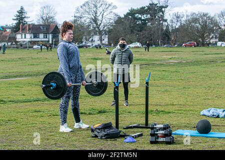 WIMBLEDON LONDON, UK 13 March 2021.  Cara exercises outdoors using weights is watched by her trainer Matthew on Wimbledon Common during lockdown on a cold blustery day. The government has started to relax lockdown restricitons allow people to meet and exercise outdoors as part of the roadmap to get back to normal life Credit amer ghazzal/Alamy Live News