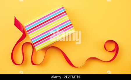 wrapped gift box and red ribbon on yellow paper background, top view Stock Photo