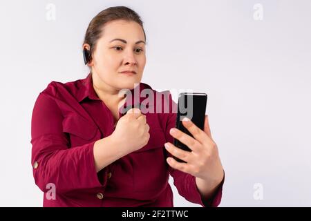 Angry businesswoman speaking on loudspeaker through smartphone, shouting or screaming and raising fist gesture. Technology, phone and human emotion Stock Photo