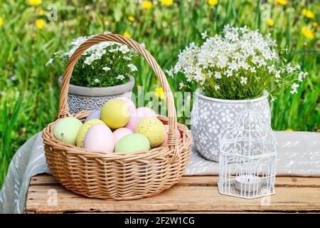 Basket of Easter eggs, traditional cakes and flowers in the garden. Outdoor party. Stock Photo