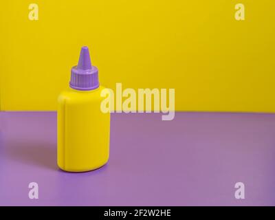 Yellow bottle with purple cap stands on purple table with yellow background. Stock Photo