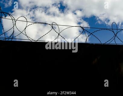Stone wall with barbed wire against blue sky. Place for text Stock Photo