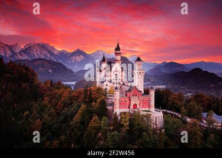 Red sky evening with castle. Beautiful sunset view of the Neuschwanstein fairy tale castle, bloody clouds with autumn colours in trees, twilight night Stock Photo