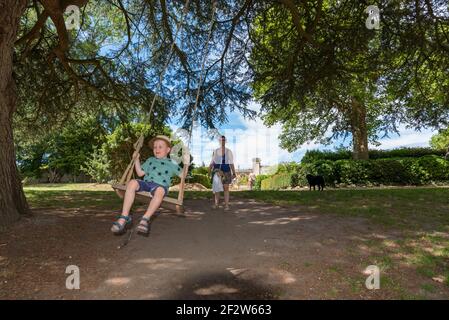 A little boy swinging on a rope swing suspended from the branch of a tree. Stock Photo