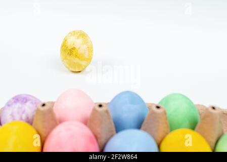Focus on golden Easter egg decorated with glitter. Easter eggs on a white background. Blurred colorful Easter eggs in front of Stock Photo