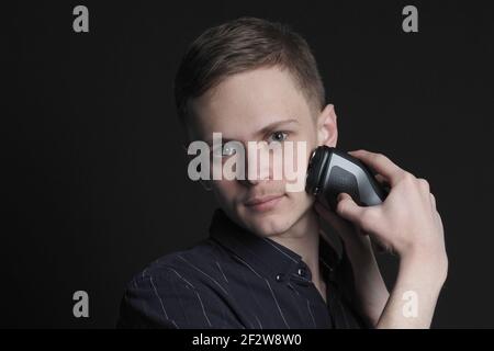 Facial. A young man shaves his face with an electric razor. Stock Photo