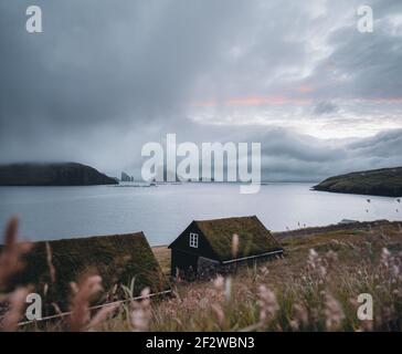 Bour village Grass-covered picturesque houses at the Faroese coastline in the village Bour with view onto Dranganir and Tindholmur during spring. Stock Photo