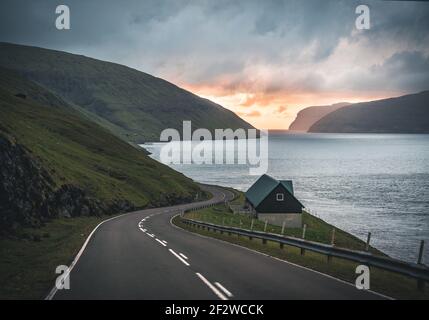 View towards street and small house with pink sky during sunset. Turf houses in Faroe islands. Stock Photo