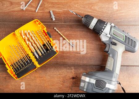 A flat lay home DIY repair concept image with a hand held drill and a set of drill bits as well as two screws and a peg on wooden background. Versatil Stock Photo