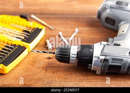 An angled home DIY repair concept image with a hand held drill and a set of drill bits as well as two screws and a peg on wooden background. Versatile Stock Photo