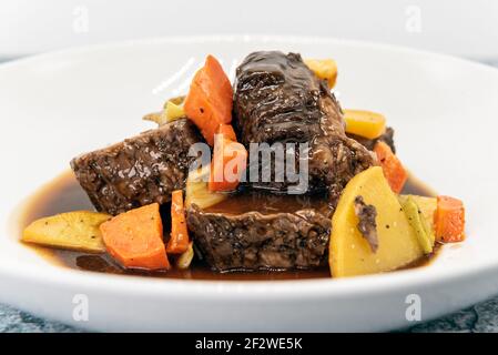 Beef short ribs drenched in a sauce and covered in carrots on other root vegetables. Stock Photo