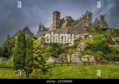 Trees and meadow at foothill of Rock of Cashel, known as Cashel of Kings or St. Patricks Rock with dramatic storm clouds, County Tipperary, Ireland Stock Photo