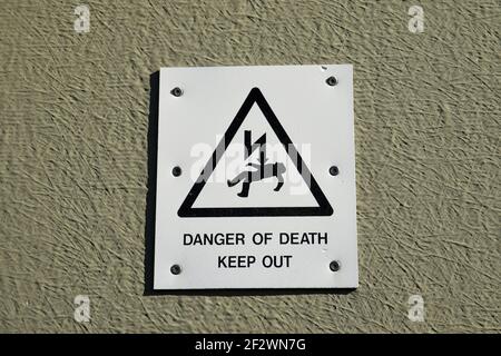 Danger of death keep out sign with icon of person being electrocuted in warning triangle. isolated against neutral coloured wall. Stock Photo