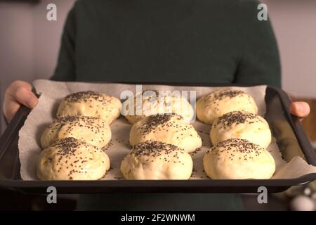 yeast dough ready for making homemade buns is on the table among other ingredients for baking bread. a woman prepares pastries, sifts flour Stock Photo