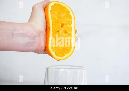 Female hand squeezing half of fresh citrus orange juice under transparent glass, healthy breakfast natural drink Stock Photo