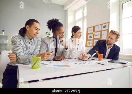 Smart diverse company employees sitting at an office desk discussing a project at a meeting. Stock Photo