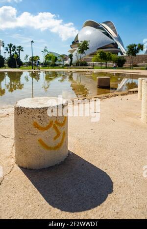 Street art in the Jardi del Turia, Valencia. A concrete block decorated with a smiling face in front of the futuristic Palau de les Arts Reina Sofia Stock Photo