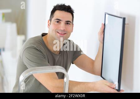 male carpenter hanging picture frame on wall Stock Photo