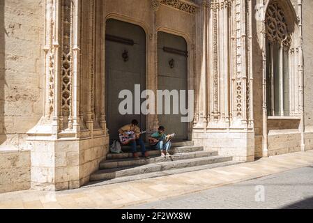 Two buskers are playing guitar sitting on the steps of an old church in the city of Valencia, Spain Stock Photo