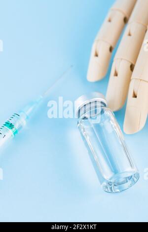Vaccine, syringe and wooden human hand. Medical ampoule and syringe on blue background. Health care and disease prevention concept. Top view Stock Photo