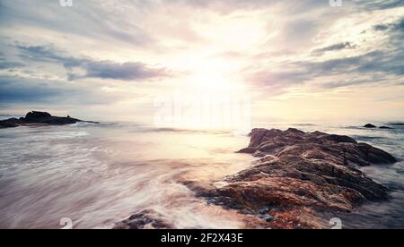 Scenic sunset on a rocky beach in Bentota, color toning applied, Sri Lanka. Stock Photo