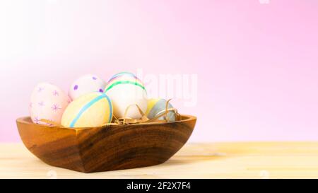 Colorful easter eggs on a wooden plate on a table on a pink background. Stock Photo