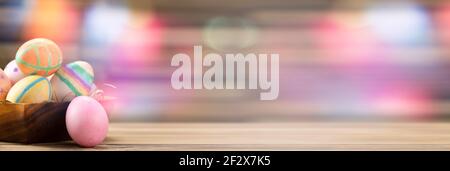 Colorful easter eggs on a wooden plate on a table on a pink background. Stock Photo