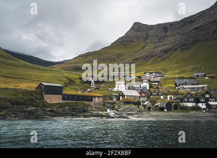 Bour village Grass-covered picturesque houses at the Faroese coastline in the village Bour with view onto Dranganir and Tindholmur during spring. Stock Photo