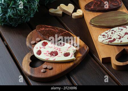 Two bitten 2D Easter eggs (ovos de Pascoa) on a heart-shaped plate. Next to chocolate callets, other 2D eggs and small wooden hearts. Stock Photo