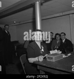 Late 1940s, historical, by the clockroom area in a cellar or basement cllub or bar, a mature lady cashier sitting at a table with a 'La Palina De Luxe' cigar box counting dollar notes, as the customers behind her enjoy a drink and a laugh. A famous brand of American cigars made by the Congress Cigar Company and run by Sam Paley, father of CBS founder, William S. Paley, the brand was created in Chicago in the mid 1800s. The La Palina is a derivative of 'the female Paley and Sam Paley's wife, Goldie Drell Paley appeared in Spanish costume on the box. Stock Photo