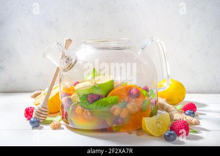 Fruit and berry tea in teapot. Hot drink with lemon, mint, blueberry, ginger, orange, apple. Hot flavored steam beverage on white wooden background co Stock Photo