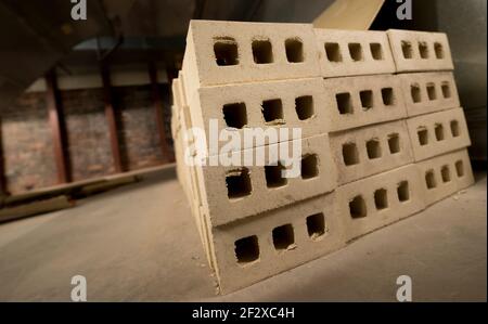 Small stack of light beige bricks indoors. Low angle, slanted, closeup view. Shallow depth of field. Concrete floor old brick wall in background. Stock Photo