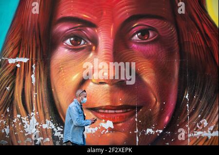Madrid, Spain. 13th Mar, 2021. A man walks past a mural in Gran Via street wearing a face mask to stop the spread of coronavirus. According to the epidemiological report of covid-19 of the Community of Madrid, the new cases of coronavirus registered in Madrid have risen to 1,500, compared to 1,301 notified yesterday, and the deaths have also increased to 27 compared to 16 on Friday. Credit: Marcos del Mazo/Alamy Live News Stock Photo