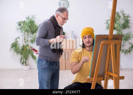 Young man taking lesson from experienced painter Stock Photo
