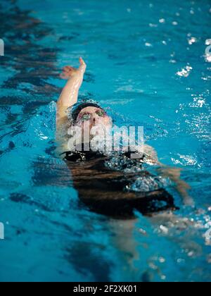A female backstroke swimmer comes to the surface in a race in an ...