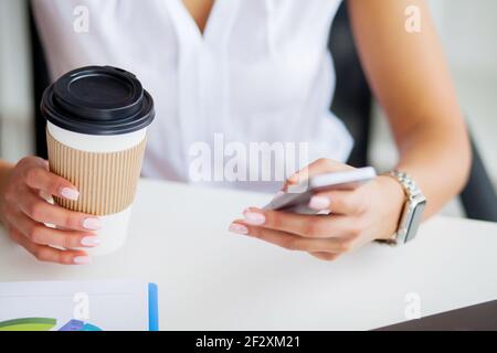 Young woman using her phone and drink coffee in office Stock Photo