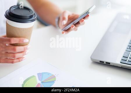 Young woman using her phone and drink coffee in office Stock Photo