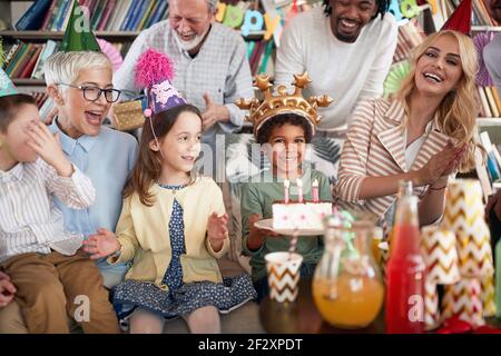 A happy little boy posing for a photo holding a cake at his birthday party in a festive atmosphere at home with family and friends. Family, celebratio Stock Photo